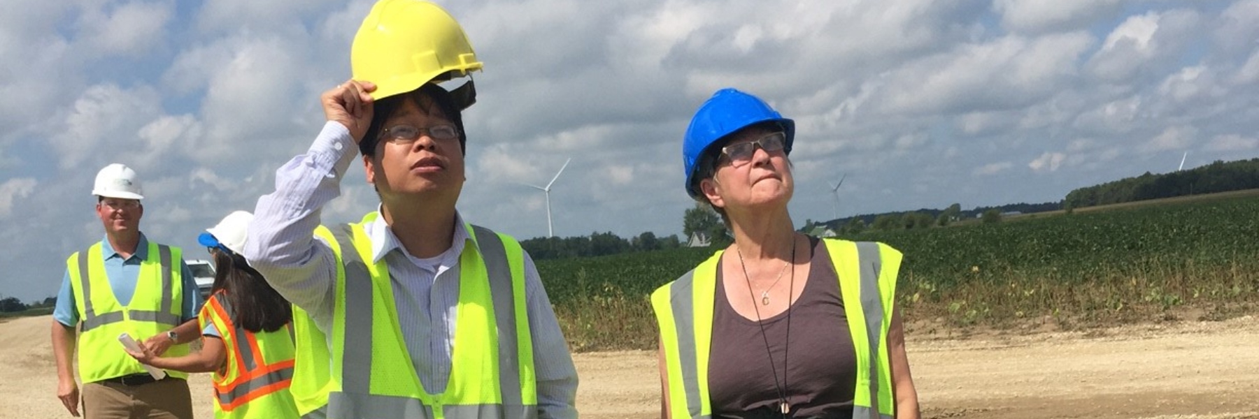 People in vests and hardhats standing in front of wind turbines
