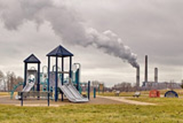 a playground that is near an industrial plant that is currently emitting some form of smoke into the air