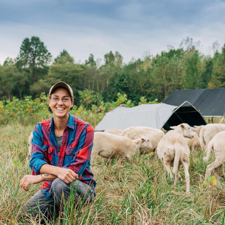 Liz Brownlee kneeling in front of some sheep and crops